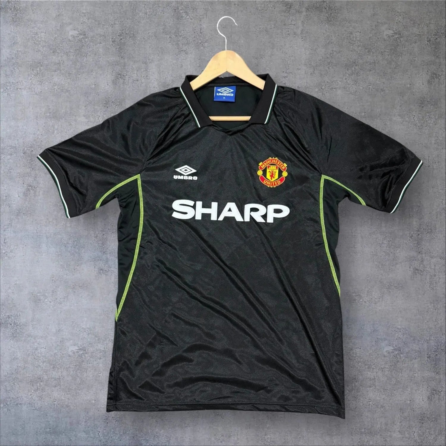 Black sports jersey with Manchester United logo and 'Sharp' branding on a hanger against a grey background